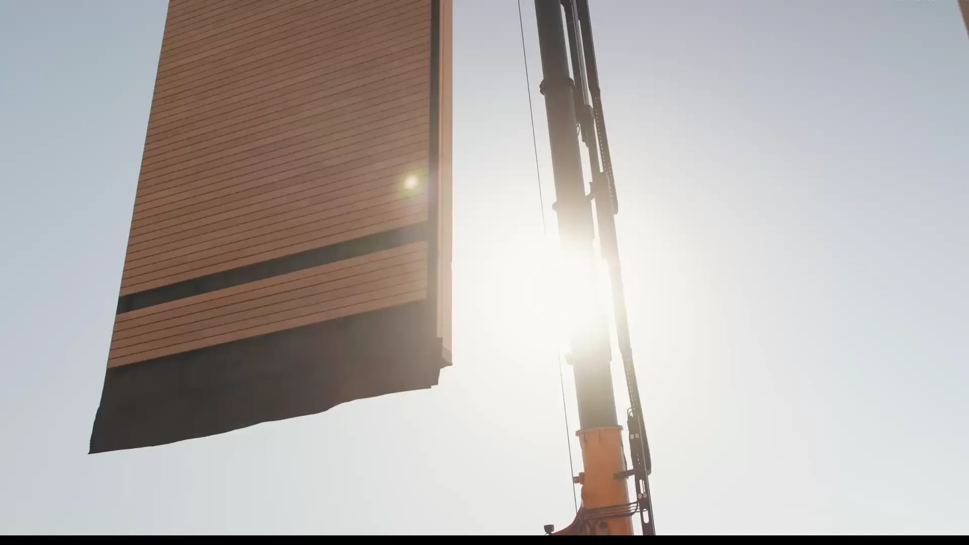 Kran hebt ein vorgefertigtes Wandelement mit Holzfassade auf die Baustelle einer Holzhalle