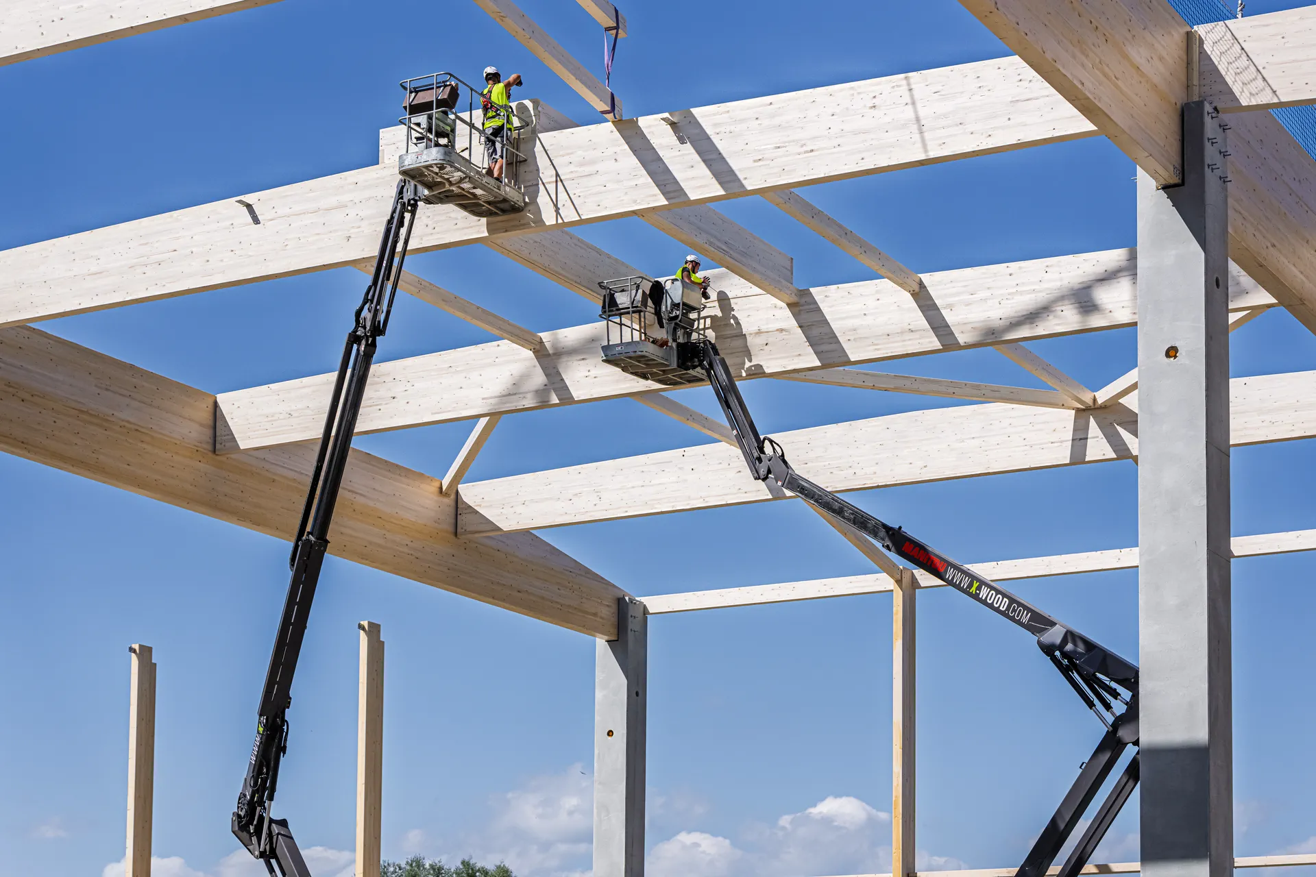 Zwei Monteure von X-Wood® setzen im Hubsteiger die Dachträger einer Holzhalle