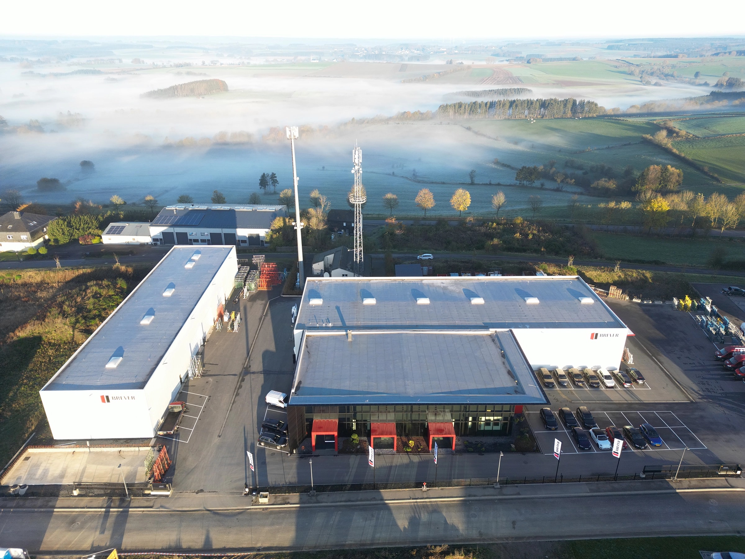 Luftaufnahme zweier Holzhallen von X-Wood® mit gläsernem Bürogebäude im Morgennebel
