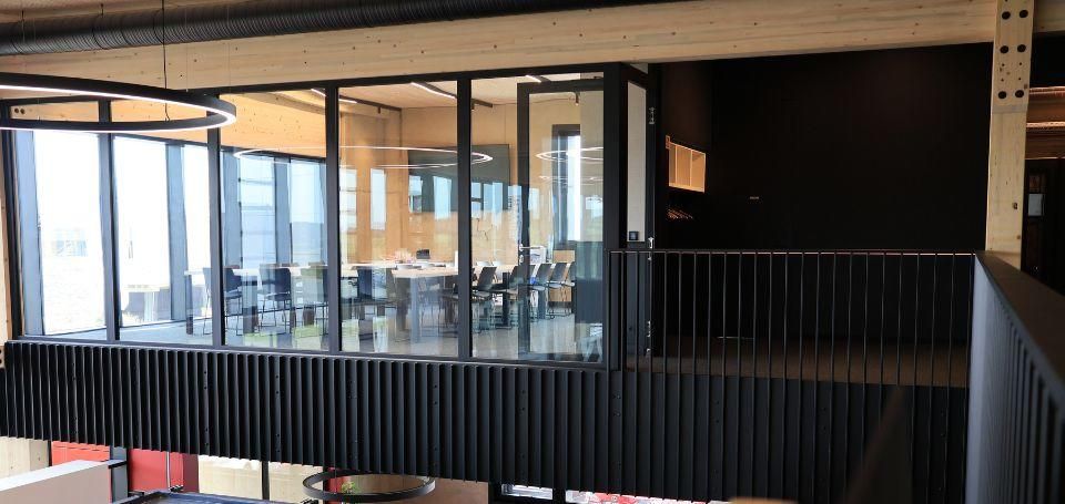 Verglaster Besprechungsraum auf der Empore einer Halle mit Büro, darüber die Hallendecke aus Holz