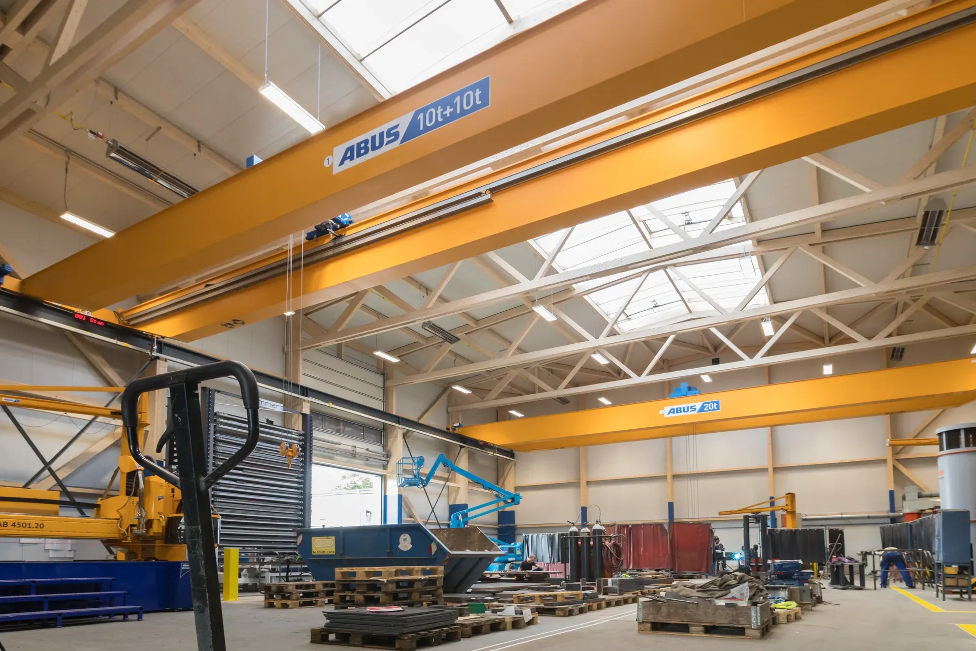 The CFM Schiller workshop hall in Roetgen with two yellow Abus crane runways, a white-glazed lattice roof and a wide light strip.