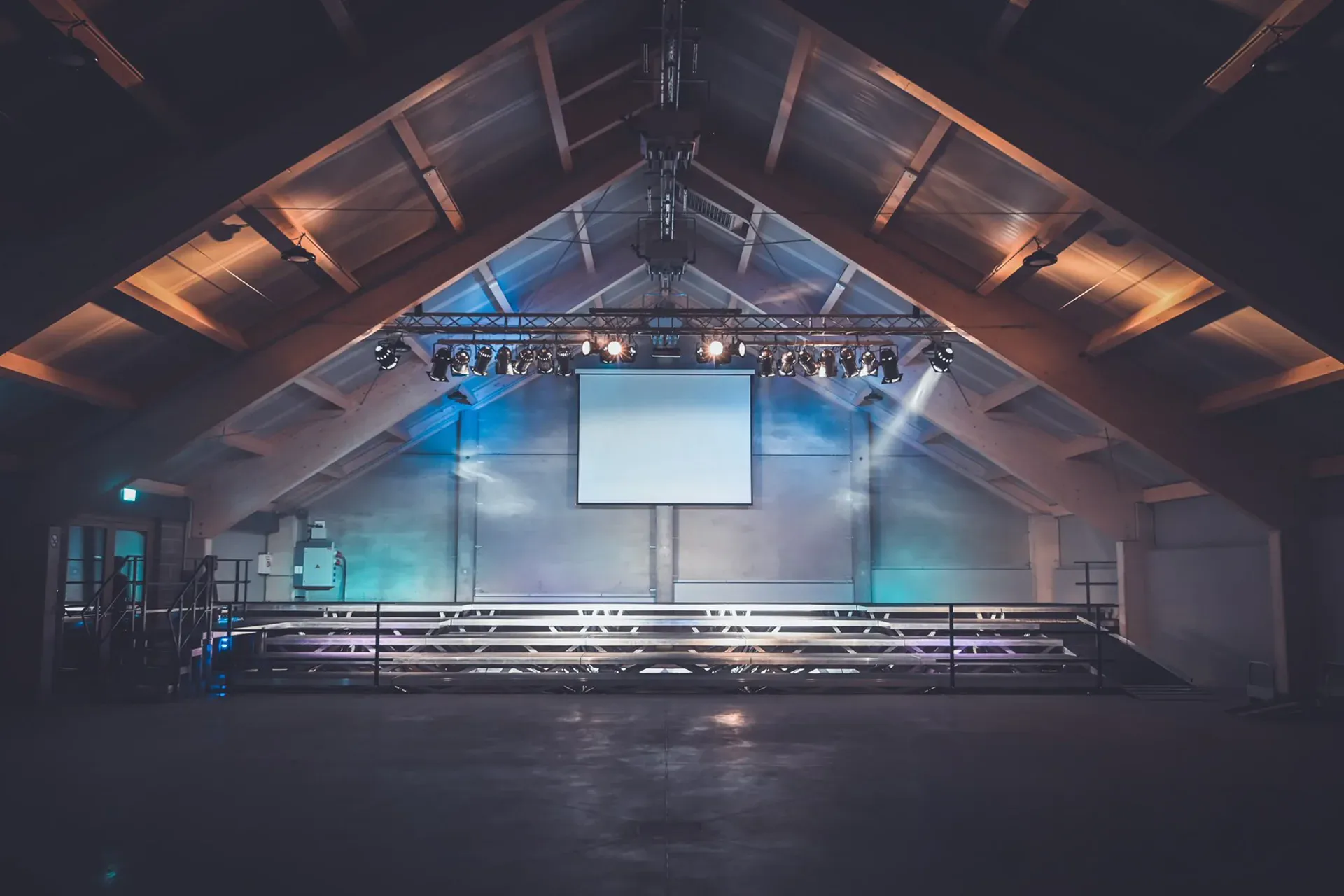 Oudler village hall in event lighting: trusses with spotlights under the timber gable roof, a screen and extended grandstand.