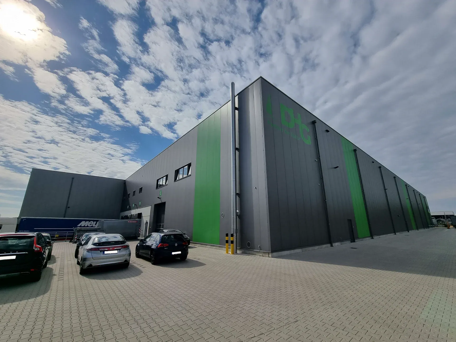 Exterior view of the DHG hall in Wachtendonk, with a grey-green trapezoidal sheet façade and the DHG logo on the gable end.