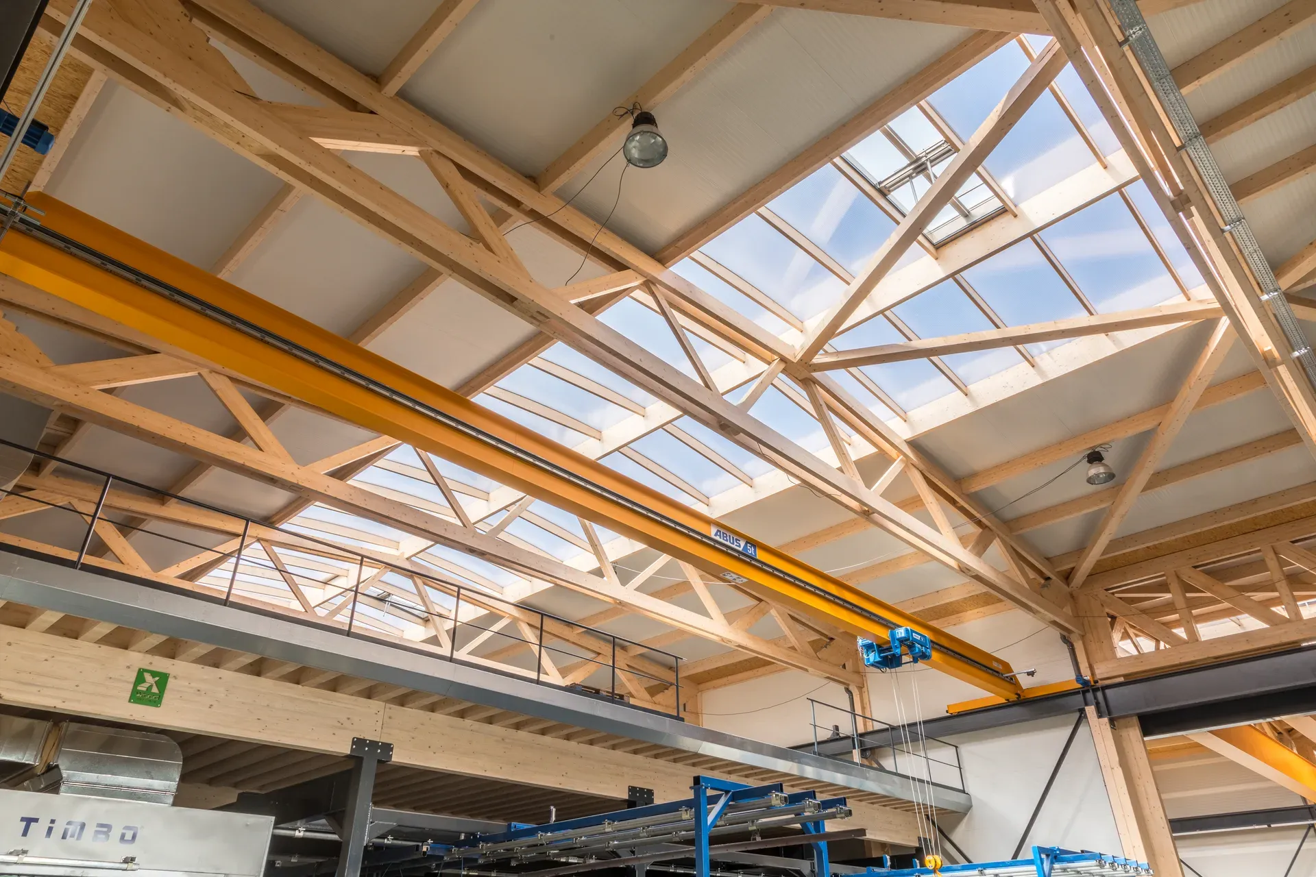 Blick in das Fachwerkdach der EMZ-Halle in Merlscheid mit Lichtfirst und gelber Abus-Kranbahn unter den Holzbindern.