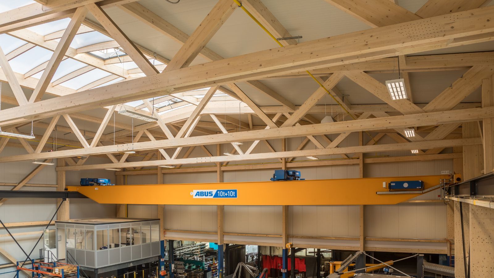 Blick in eine Produktionshalle mit Holztragwerk und Krananlage unter einem Dach mit Lichtbändern