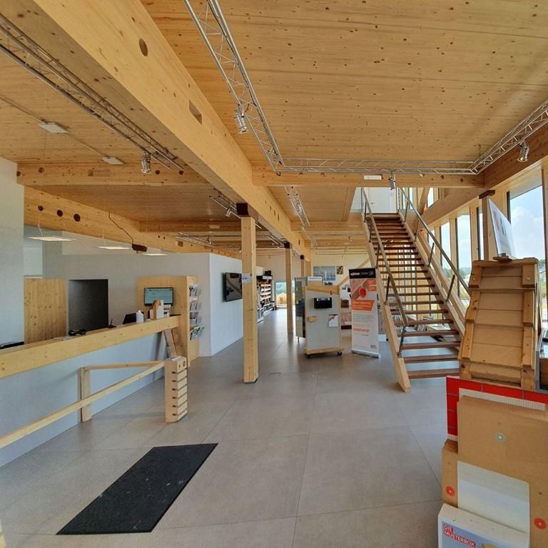 Empfang und Ausstellungsfläche im Bürotrakt einer Holzhalle mit Brettschichtholz-Decke und Treppe zur Empore