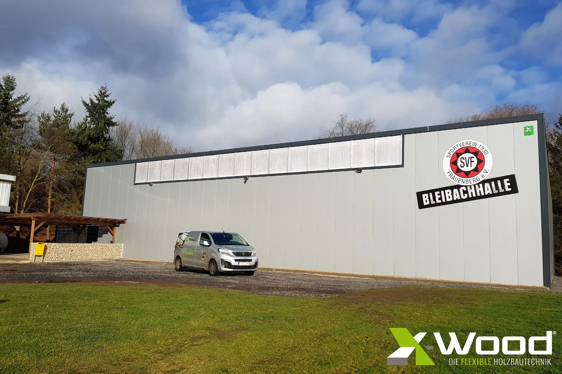 Exterior view of the SV Frauenberg Bleibachhalle in Euskirchen with the club crest, the hall lettering and an X-Wood® company vehicle in front.