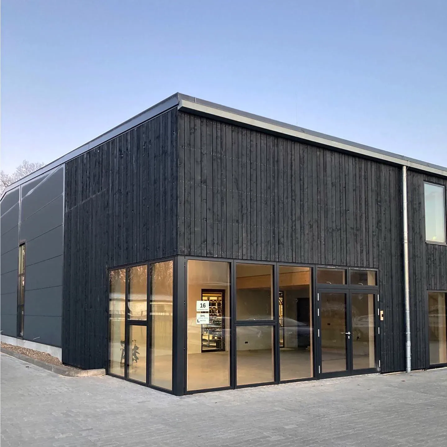 The Jan Cray commercial hall in Radbruch with a black timber façade, a glazed building corner and the adjoining grey hall wall.