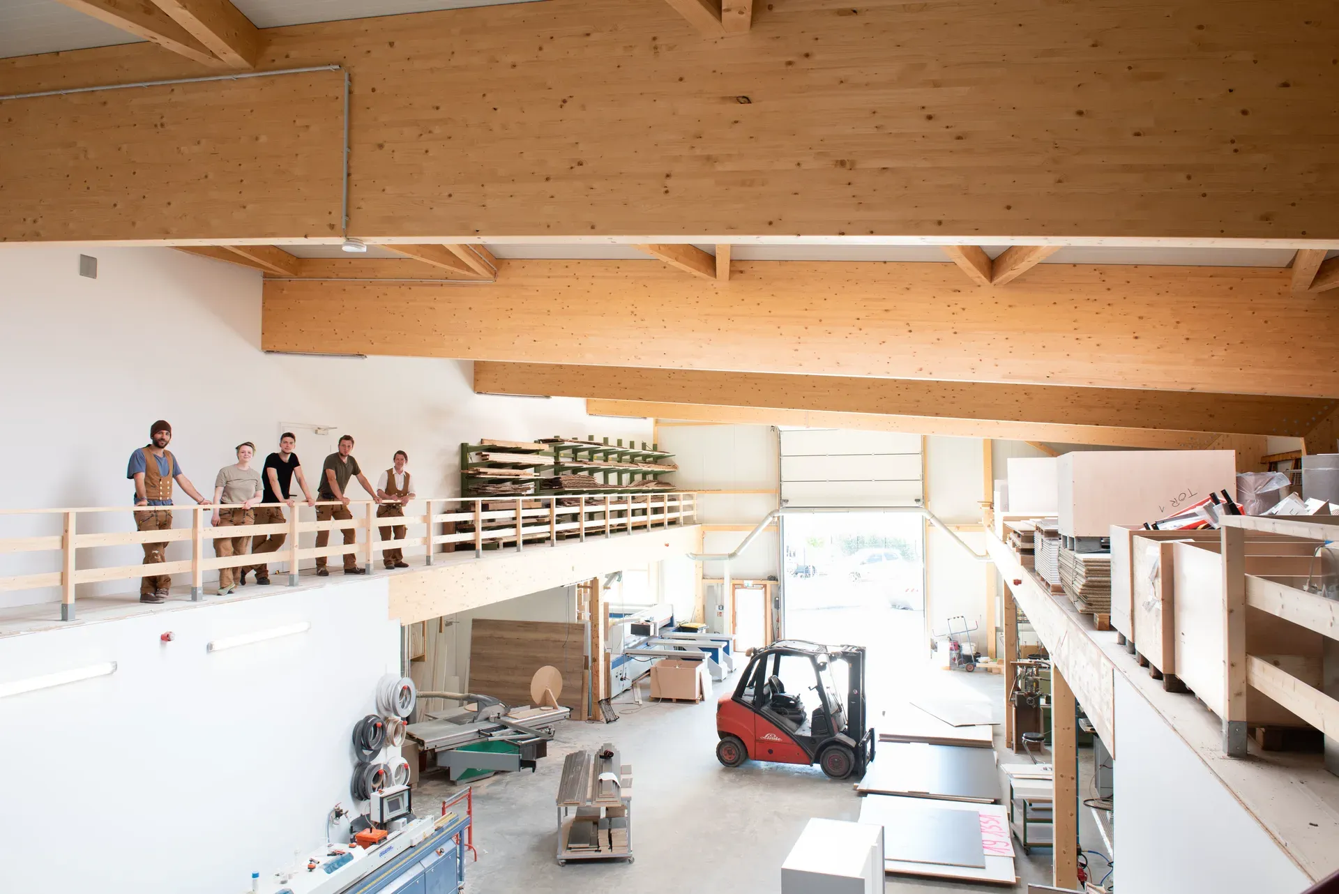 The Treibgut joinery team on the mezzanine of the hall in Herten, with the workshop and a forklift below under exposed glulam trusses.