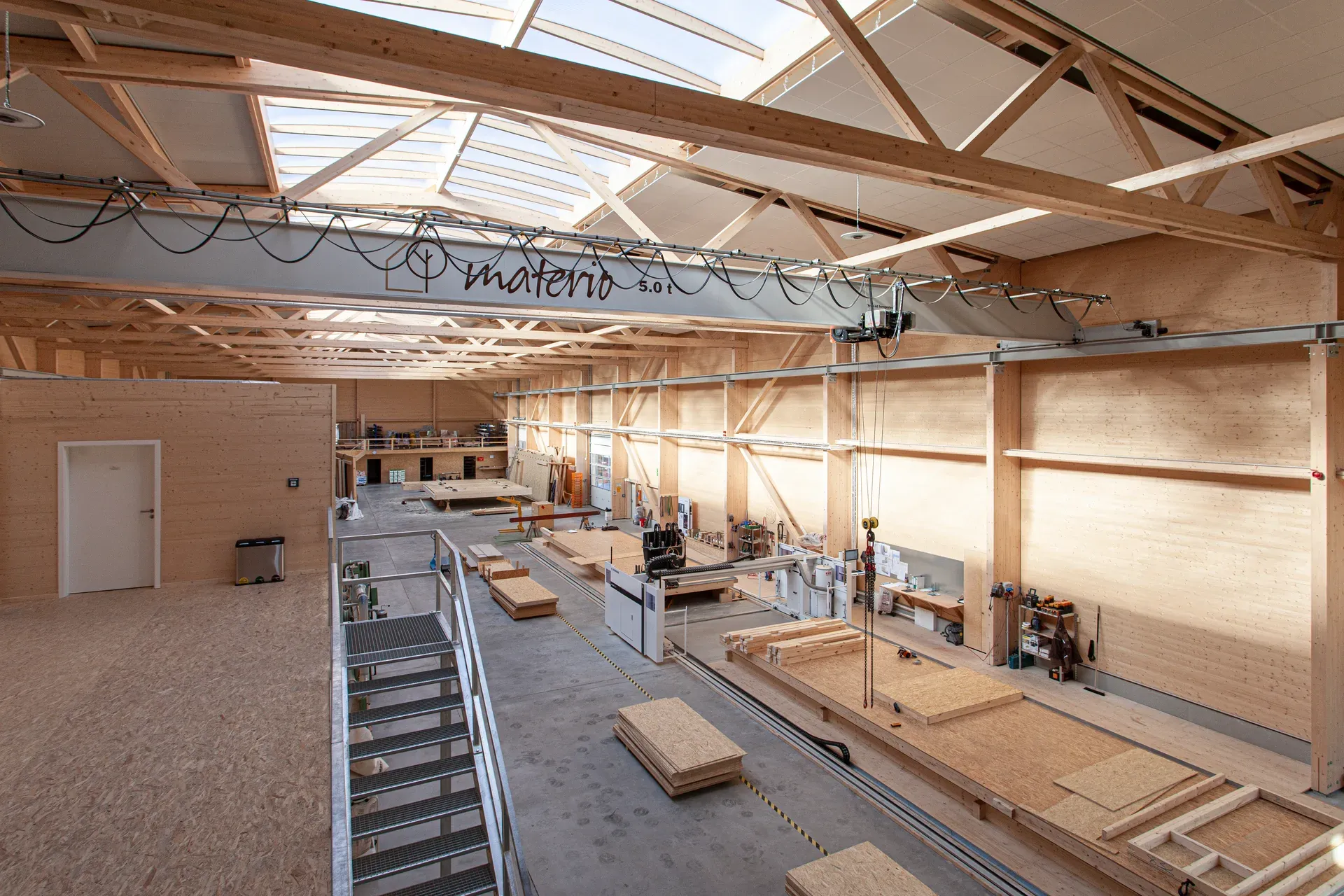 The materio production hall in Soest, with an exposed timber structure, wide roof light strips, the materio lettering on the truss and the workshop below.