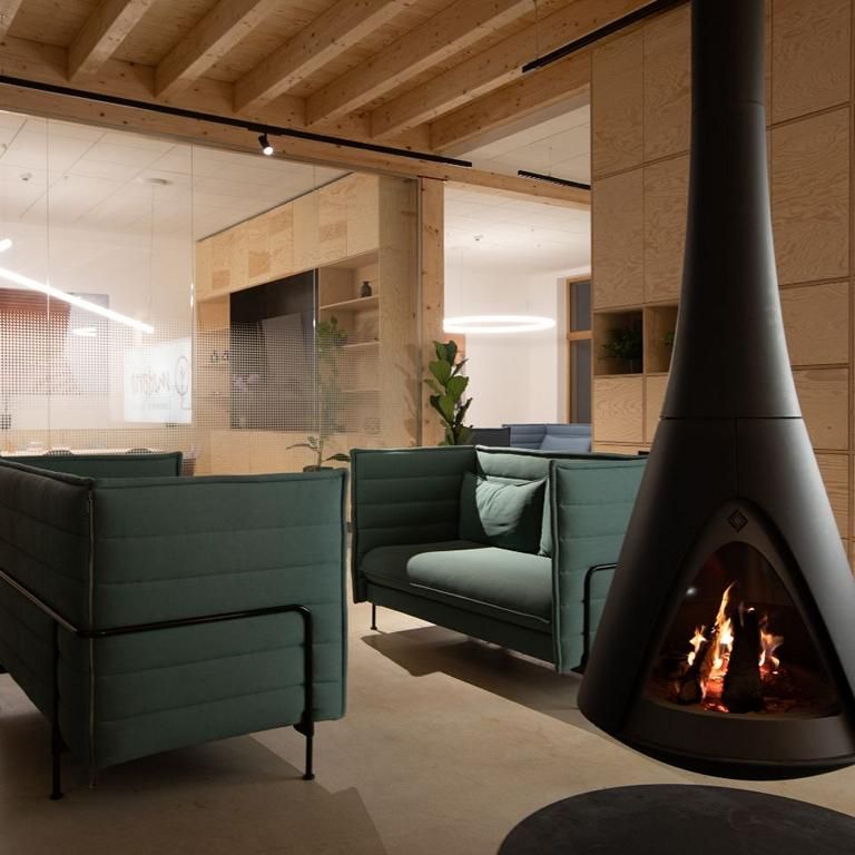 Sitzecke mit Kamin im Bürobereich einer Holzhalle unter der sichtbaren Balkendecke