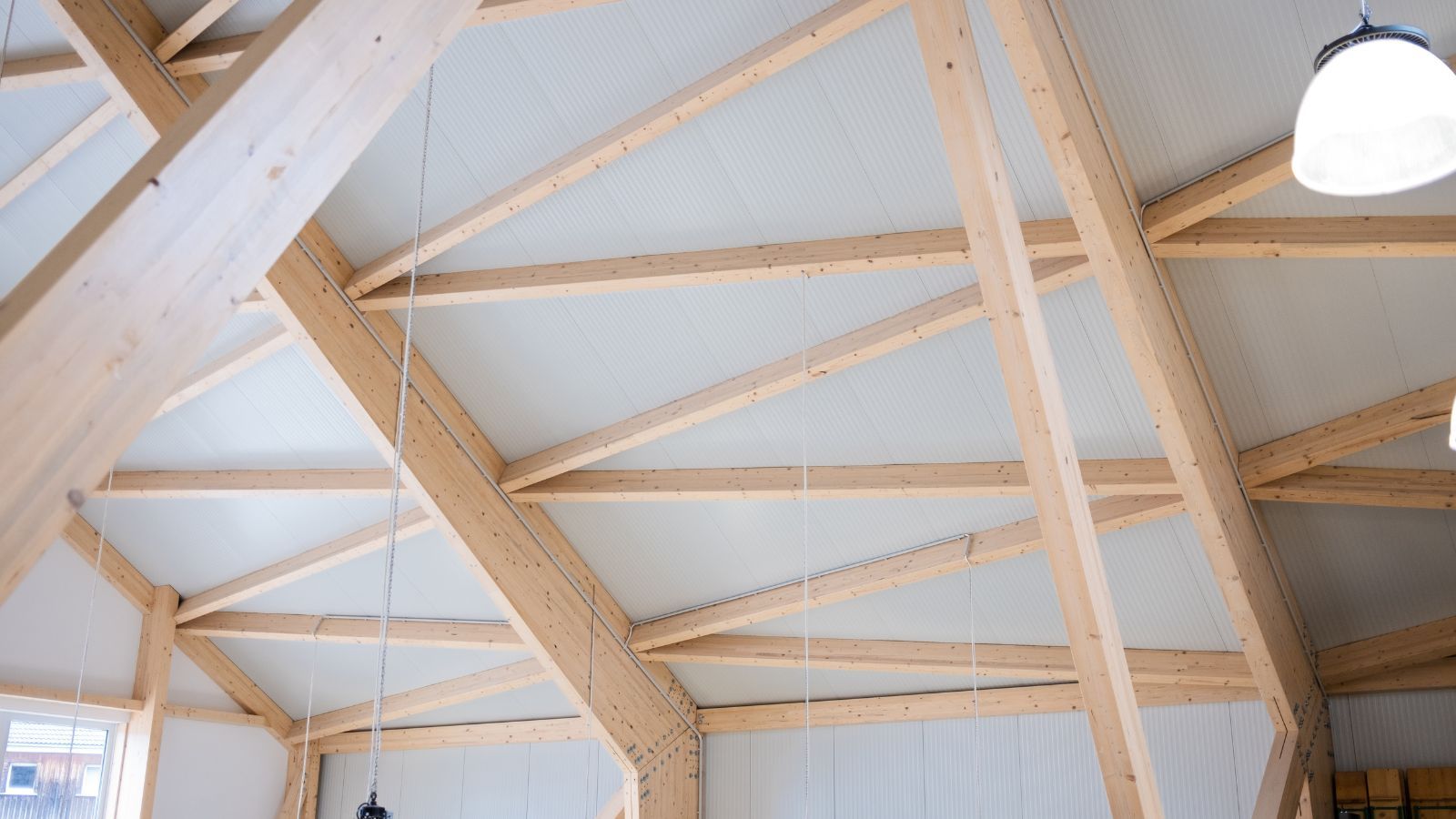 Nahaufnahme eines Dachtragwerks aus Holz in einer modernen Halle mit weißen Sandwichpaneelen