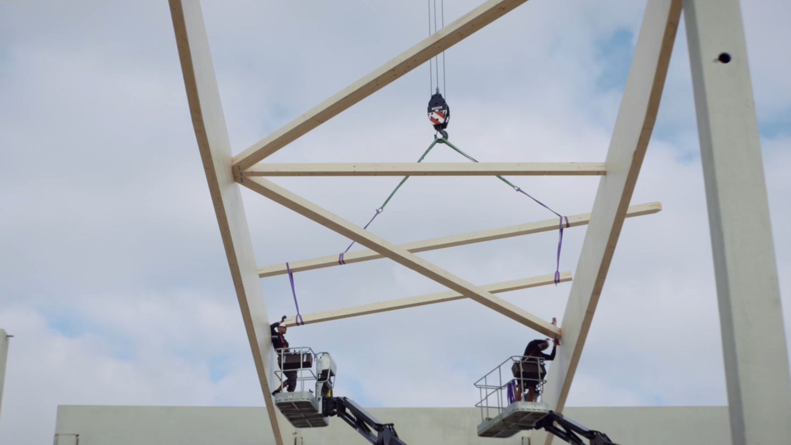 Montage eines Holztragwerks mit Kran und zwei Hebebühnen auf einer Baustelle.