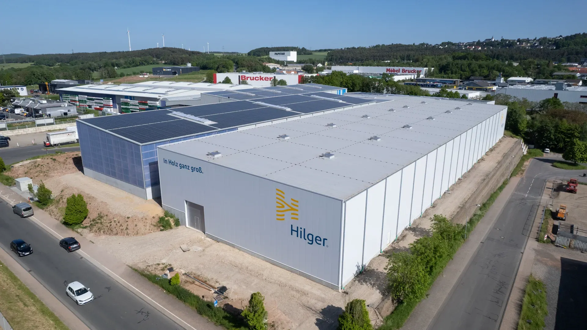 Luftaufnahme der Lagerhalle von Hilger Holz in Kall mit Photovoltaikdach und Hilger-Logo auf der weißen Längsseite.