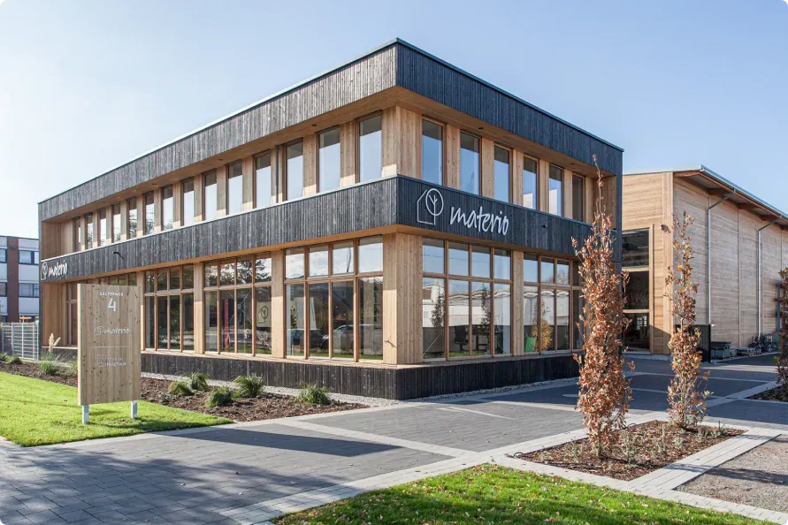 Außenansicht des zweigeschossigen materio-Bürogebäudes in Soest mit Holzfassade, Fensterbändern und Firmenlogo.
