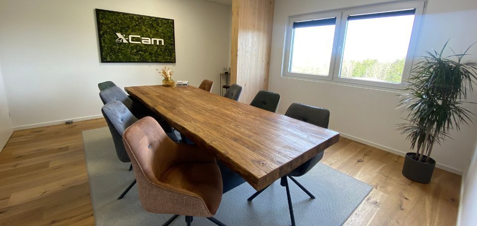 Besprechungsraum im Büro einer X-Wood®-Halle mit massivem Holztisch und Mooswand mit X-Cam-Logo